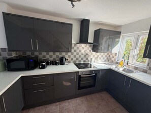 A modern kitchen with dark cabinets, a microwave, toaster, and a stove. - 2BDR House with Private Garden and Parking (Greater London)
