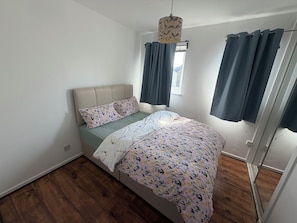 Een slaapkamer met een bed, een raam met gordijnen, een hanglamp en houten vloeren.