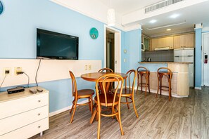 Ein Essbereich mit rundem Tisch und Holzstühlen, einem an der Wand befestigten Fernseher und einer Küche im Hintergrund.