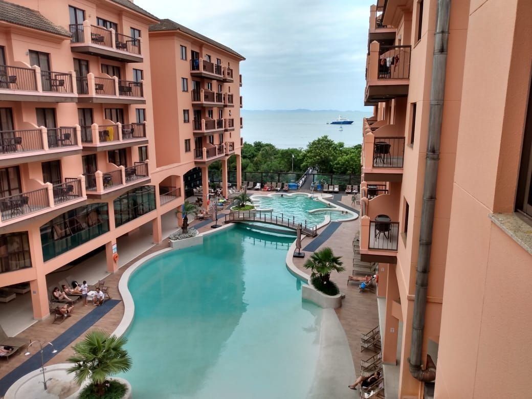 Un hotel de varios pisos con piscina central, balcones y vistas al mar.