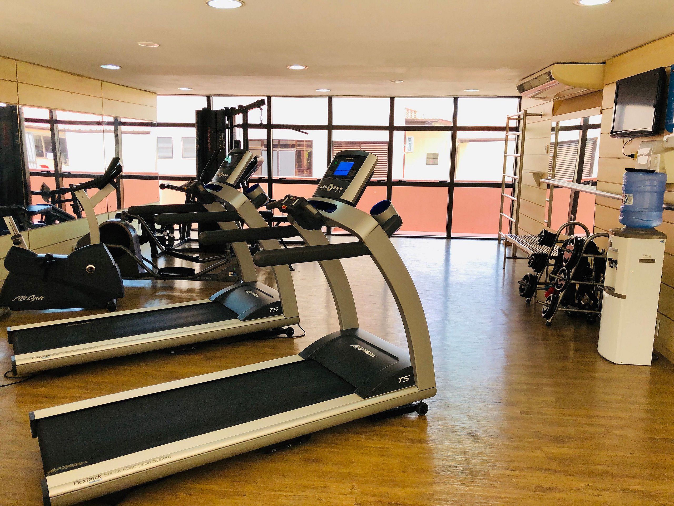 Ein Fitnessstudio mit Laufbändern, Kraftgeräten und einem Wasserspender.