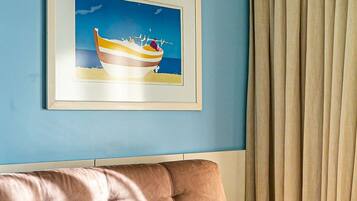 Ein Zimmer mit blauer Wand, einem gerahmten Bild eines Bootes, einem beigen Sofa und einem Vorhang.
