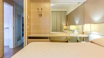 Een hotelkamer met een bed, nachtkastje, spiegel en deur naar een badkamer.