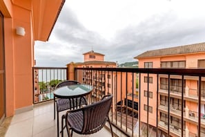 Un balcón con mesa y sillas, con vistas a un edificio que tiene varios balcones y una torre distante.