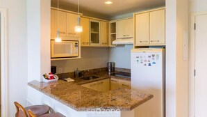 A compact kitchen with granite countertops, a microwave, a refrigerator, and wooden cabinets. - Oceanfront Suite in a Beachfront Resort Jbv122 (Florianópolis)