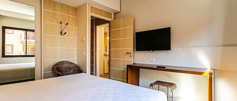 A hotel room with a bed, a desk, a TV, a chair, and a door leading to another room.