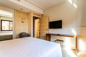 Una habitación de hotel con una cama, un escritorio, un televisor, una silla y una puerta que da a otra habitación.