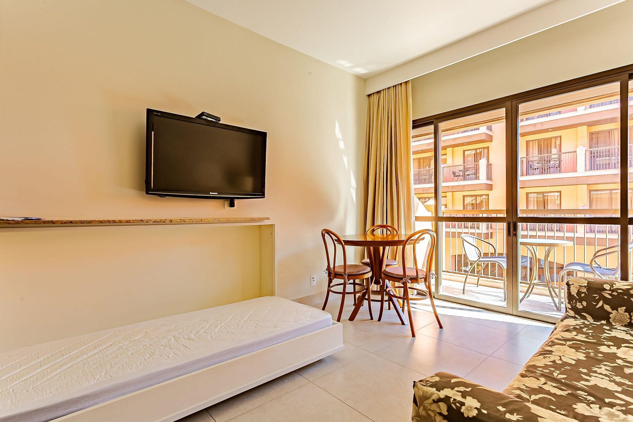 Een hotelkamer met een bed, een televisie, een eettafel met stoelen en een balkon met tuinmeubilair.