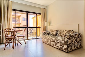 A living room with a sofa, chairs, a table, and a view through a large window. - Suite w/ Sea/pool View Luxury Resort Jurere Jbv142 (Florianópolis)