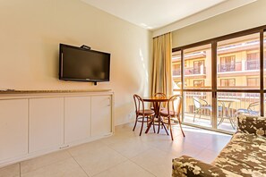 A hotel room with a TV, a dining table with chairs, a sofa, and a balcony with a view of the building. - Suite w/ Sea/pool View Luxury Resort Jurere Jbv142 (Florianópolis)
