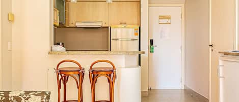 A kitchen with wooden cabinets, a white countertop, two wooden stools, and a refrigerator.