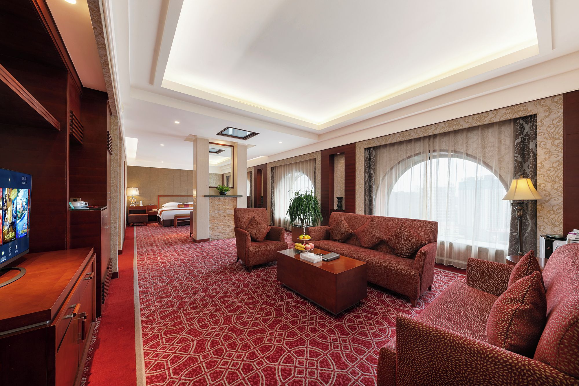 A hotel room with a large bed, a sofa, a coffee table, and a TV.