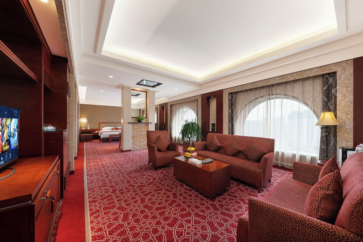 A hotel room with a large bed, a sofa, a coffee table, and a TV.