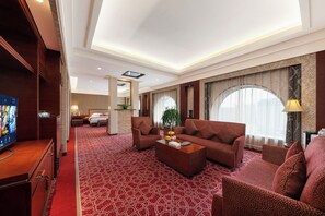 A hotel room with a large bed, a sofa, a coffee table, and a TV.