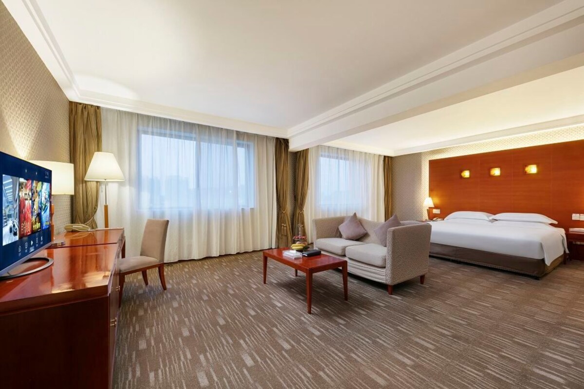 A hotel room with a bed, a sofa, a desk with a television, and a coffee table.