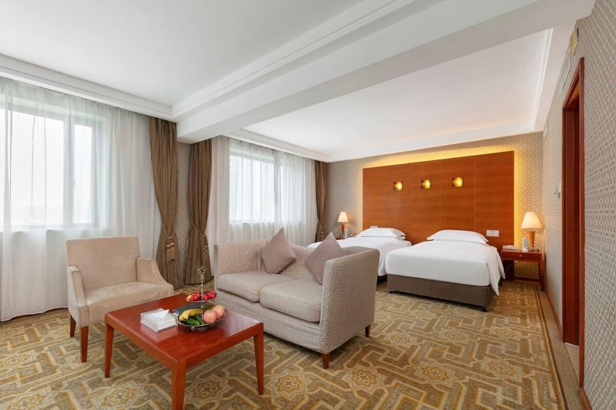 A hotel room with a sofa, a bed, a small table with fruits, and a patterned carpet.