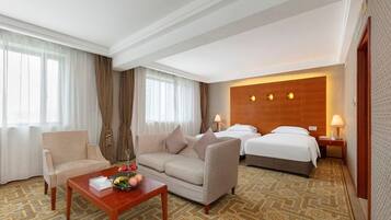 Habitación de hotel con sofá, cama, una mesita con frutas y una alfombra estampada.