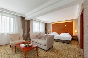 Habitación de hotel con sofá, cama, una mesita con frutas y una alfombra estampada.