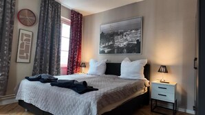 Ett hotellrum med en säng, ett sängbord, en klocka, en inramad tavla och gardiner.