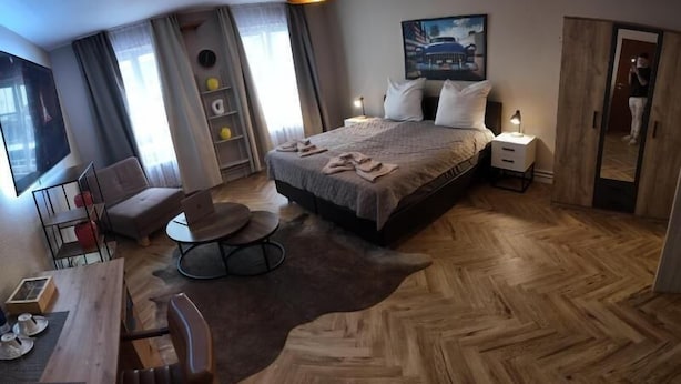 Ett hotellrum med en säng, ett skrivbord, en stol, ett runt bord och ett stort fönster.