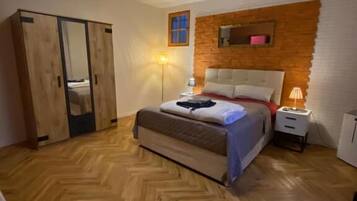 Ein Schlafzimmer mit Holzdielen im Fischgrätmuster, einem Bett mit weißem Kopfteil, einem Kleiderschrank und einem Nachttisch mit Lampe.