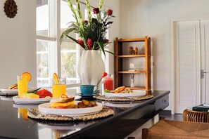 A breakfast setting with a vase of flowers, a fruit plate, a glass of orange juice, and a cup of coffee on a kitchen counter. - Coastal Garden Villa (Ungasan)