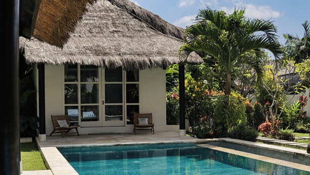 A pool area with a thatched-roof structure, two lounge chairs, and lush tropical plants. - Coastal Garden Villa (Ungasan)