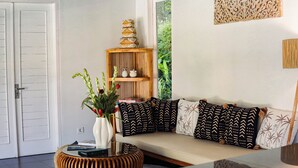 A living room with a sofa, patterned cushions, a round wooden side table, a white vase with flowers, a bookshelf, and a door. - Coastal Garden Villa (Ungasan)