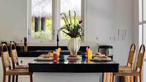 A modern kitchen with a central island, two doors leading to a garden, and a dining area with chairs and a table. - Coastal Garden Villa (Ungasan)