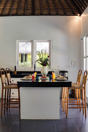 A modern kitchen with a central island, two doors leading to a garden, and a dining area with chairs and a table. - Coastal Garden Villa (Ungasan)