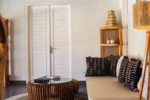 A room with a white door, a round glass table, a sofa with patterned cushions, and a wooden shelf with decorative items. - Coastal Garden Villa (Ungasan)