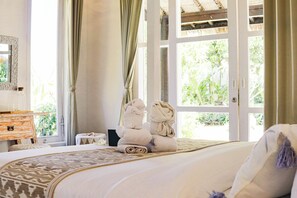 A bedroom with a large bed, a wooden dresser, a small table, and a window with curtains. - Coastal Garden Villa (Ungasan)