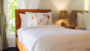 A hotel room with a wooden bed, white bedding, a nightstand with a lamp, and a view of greenery through the window. - Coastal Garden Villa (Ungasan)