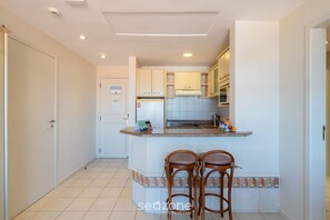 A kitchen with a central island, two bar stools, and a refrigerator. - Beachfront Resort Suite w/ Pool Jbv227 (Florianópolis)
