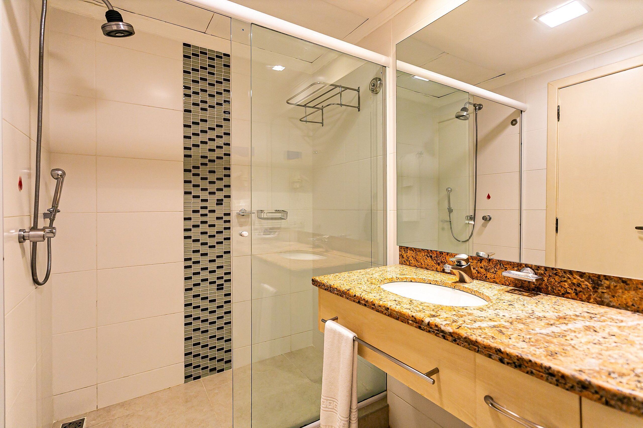 A modern bathroom with a glass-enclosed shower, a granite countertop sink, and a large mirror.