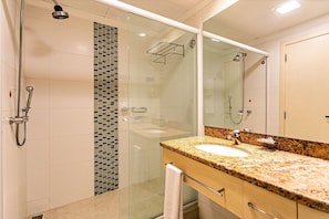 Ein modernes Badezimmer mit einer Duschkabine aus Glas, einem Waschbecken mit Granitplatte und einem großen Spiegel.