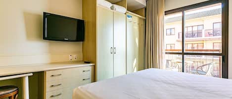 A hotel room with a bed, a desk with a chair, a wardrobe, and a television on the wall.