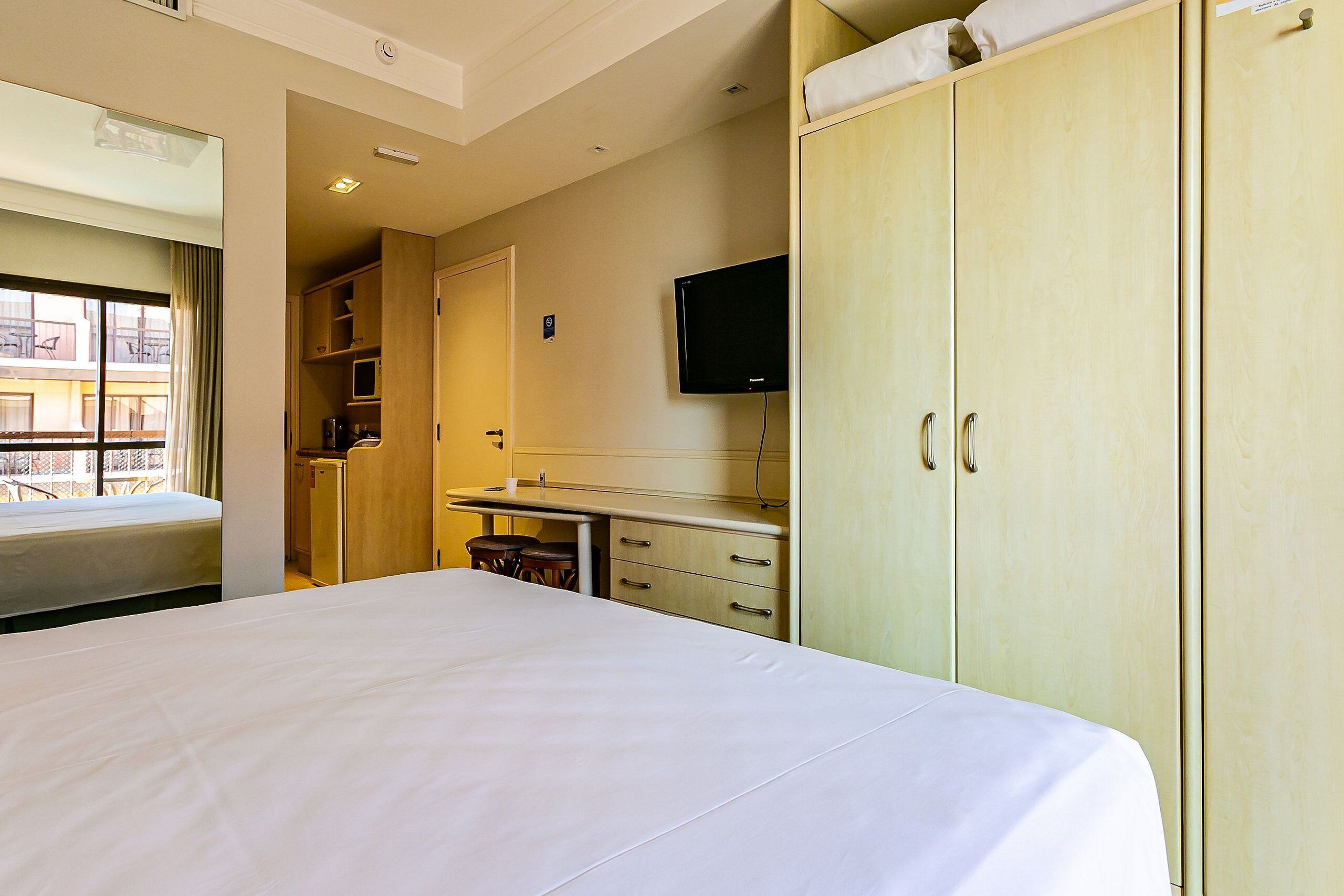 A hotel room with a bed, a desk, a television, and a wardrobe.