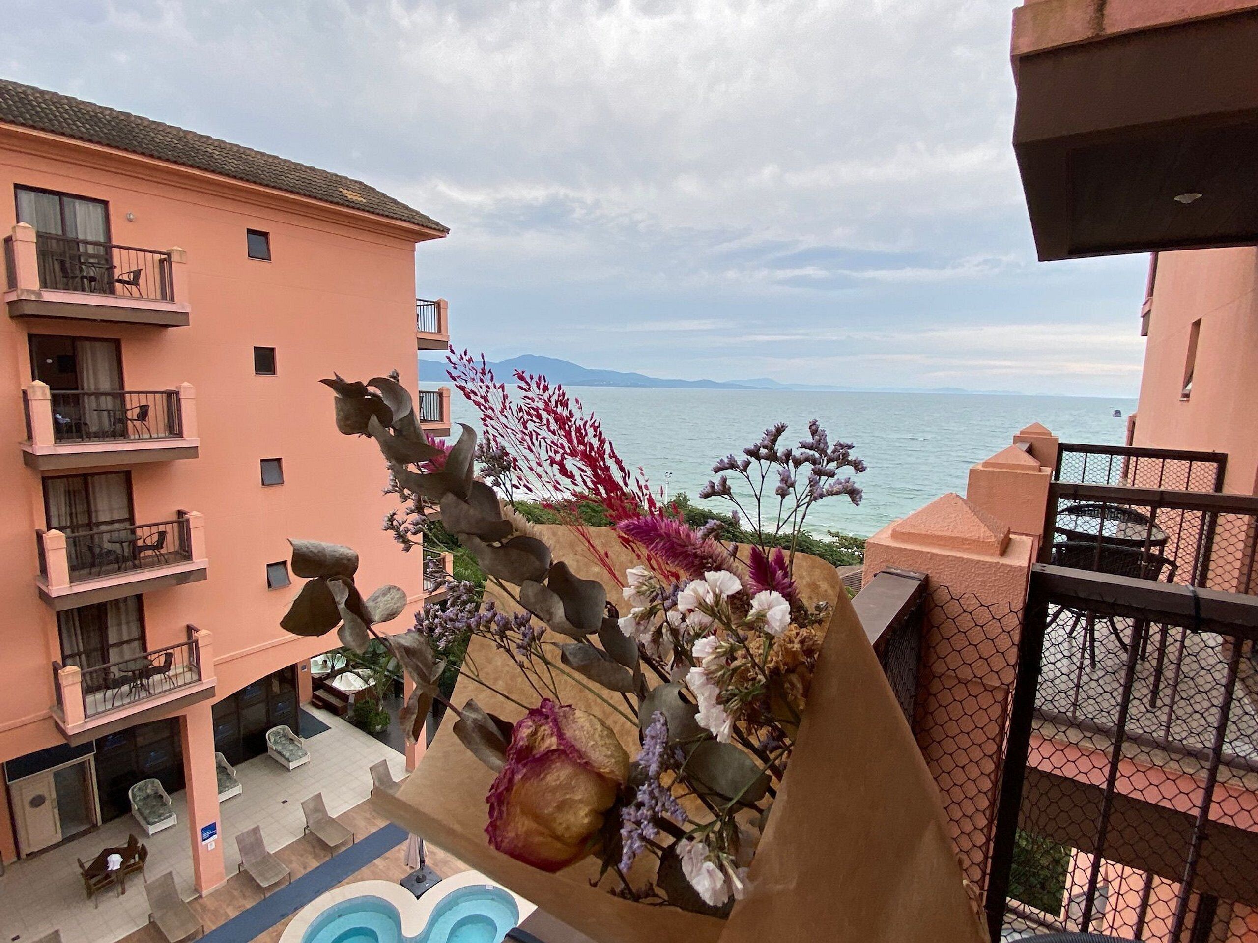 A balcony with a view of the sea, a flower arrangement, and a pool.