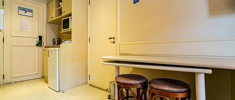 Una pequeña cocina americana equipada con refrigerador, microondas y pileta. Hay dos taburetes de madera debajo de un mostrador blanco.