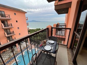 Ein Balkon mit Esstisch, Blick auf ein Schwimmbad und Meer mit Bergen in der Ferne.