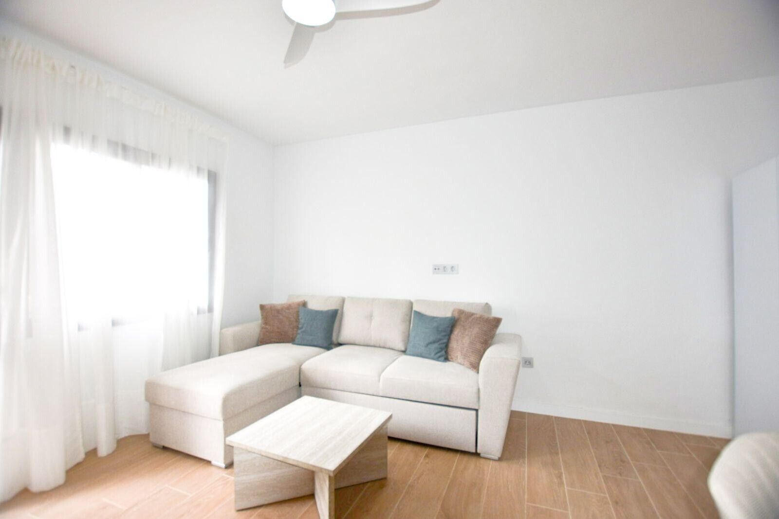 Een moderne woonkamer met een hoekbank, een klein bijzettafeltje en een plafondventilator.
