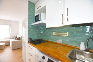 Eine kompakte Küche mit weißen Schränken, einer Holz Arbeitsplatte, einer Mikrowelle und einem Spülbecken.