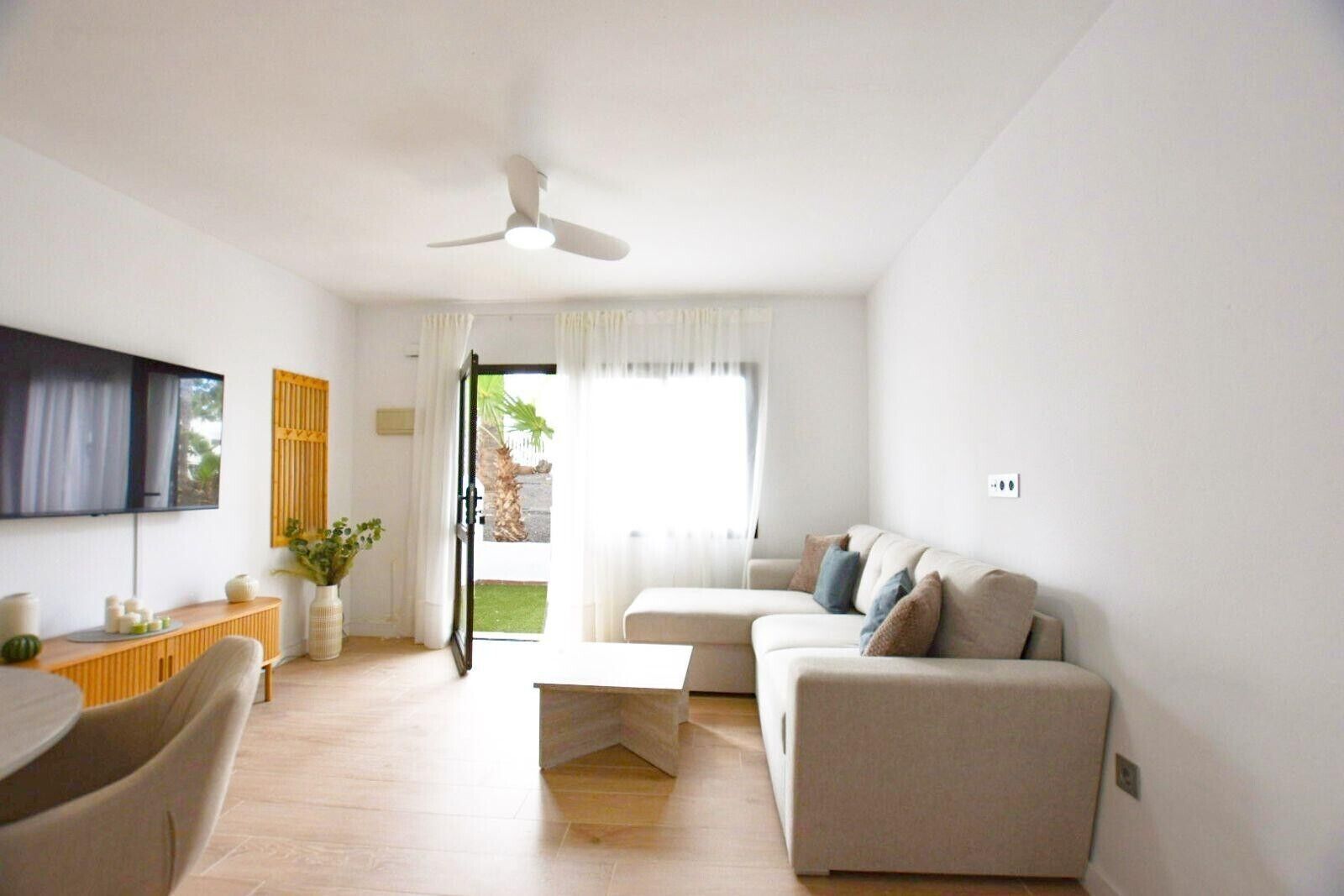 Un salon moderne avec un canapé, une table basse, un téléviseur fixé au mur et un ventilateur de plafond.