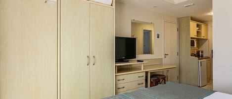 Habitación de hotel con cama, televisión, escritorio y kitchenette.
