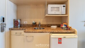 Eine kompakte Küchenzeile mit einer Mikrowelle, einer Kaffeemaschine, einem Spülbecken und einem Kühlschrank.