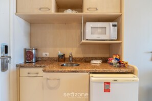 Eine kompakte Küchenzeile mit einer Mikrowelle, einer Kaffeemaschine, einem Spülbecken und einem Kühlschrank.