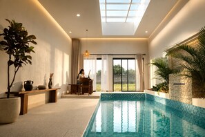 A modern indoor swimming pool with a clear view of the outdoors, a dining area with a table and chairs, and a large potted plant. - Tepa Menep Villa (Ngaglik)