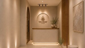 A modern interior with a reception desk, a logo above it, and three round tables with a textured surface. - Tepa Menep Villa (Ngaglik)