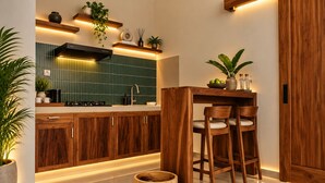 A modern kitchen with wooden cabinets, a built-in stove, and a bar area with stools. - Tepa Menep Villa (Ngaglik)